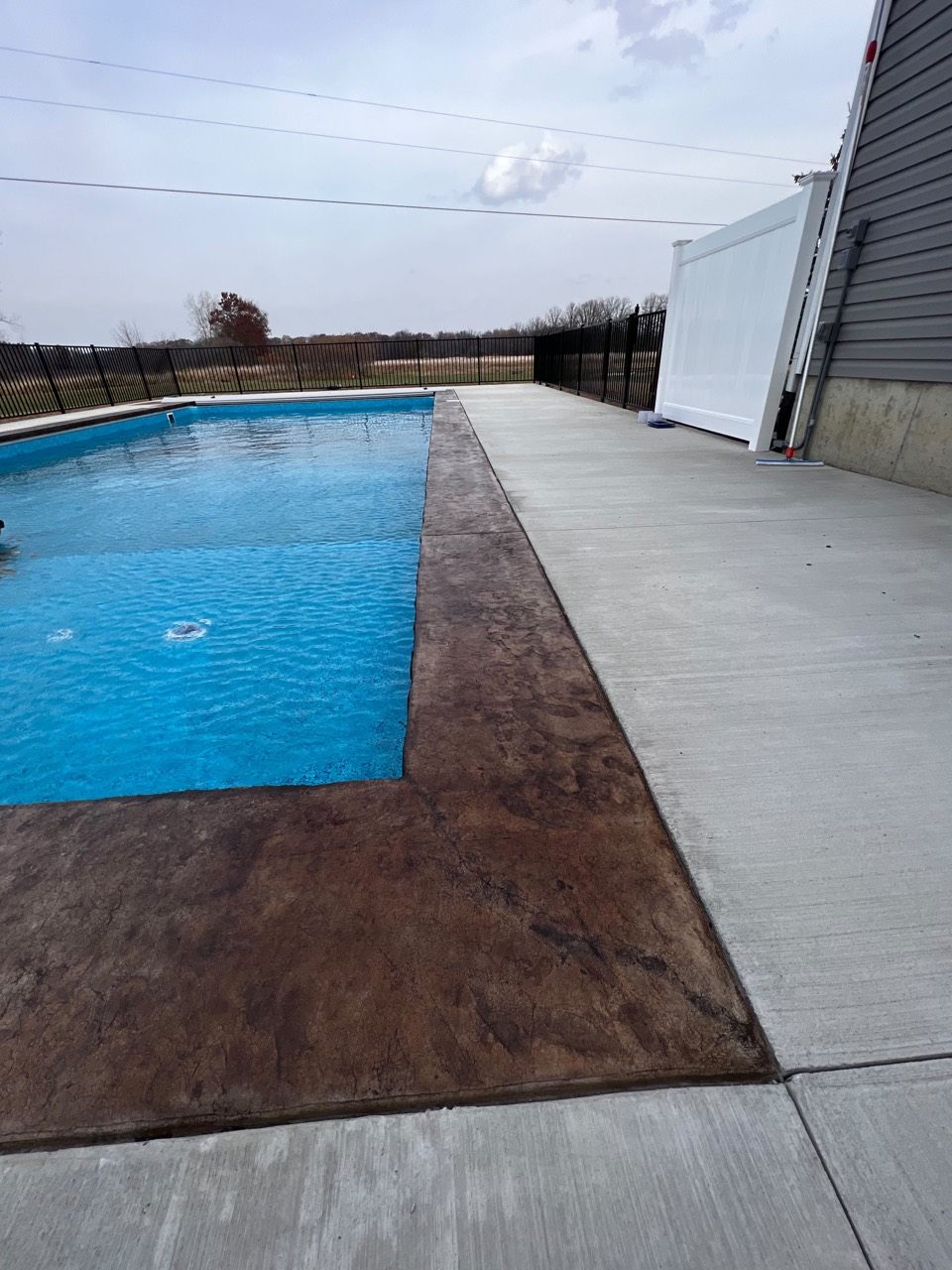 Brown textured acid-stain border alongside concrete surrounding a swimming pool